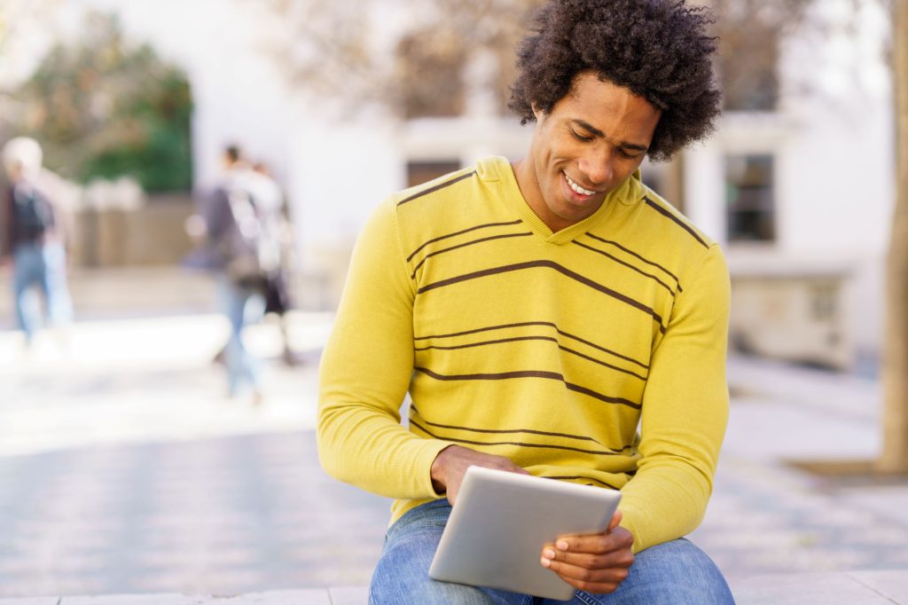 Black man using a digital tablet sitting on a benc gyrsgyu